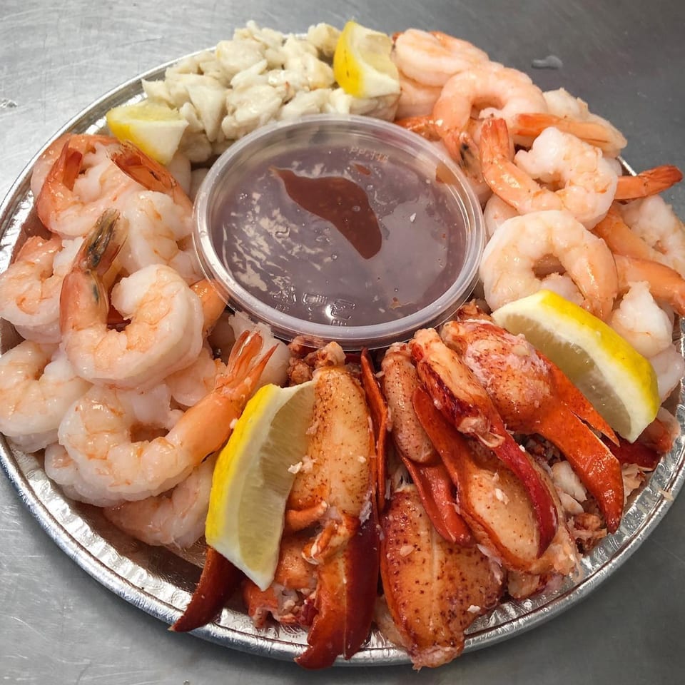 A seafood platter with shrimp, lobster claws, crab meat, lemon wedges, and cocktail sauce.